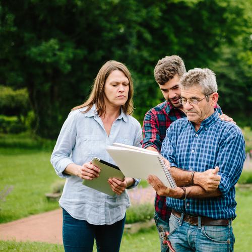 Three farmers or salespeople standing in an orchard looking at a form or sales sheet together.