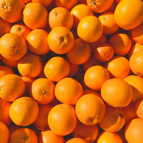 Close-up shot of hundreds of brightly colored oranges in a bin shot from overhead.