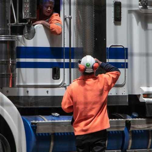 A man with safety gear is speaking with and directing a truck with a driver inside.