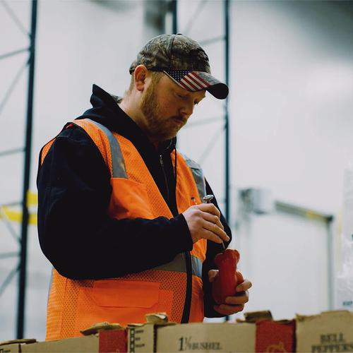 A worker in a warehouse storage facility checks the temperature of a red pepper.
