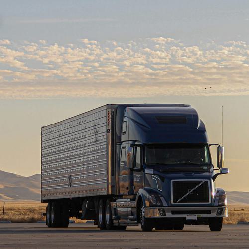 A large semi-truck in a parking lot with a mountainous sunset in the background.
